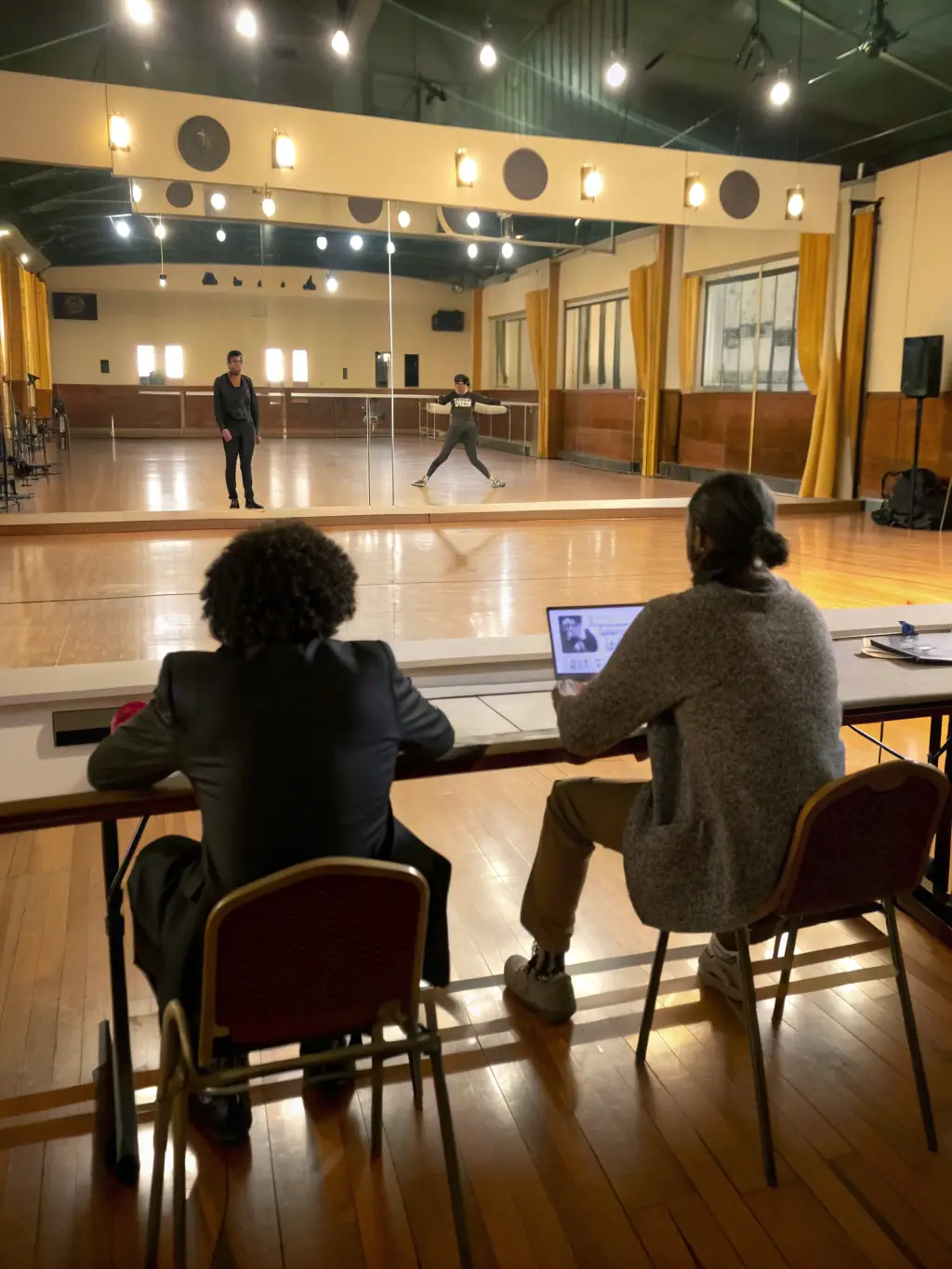 A professional photo of a panel of judges at a table, smiling as a confident student performs on stage under spotlights, for an open auditions card.